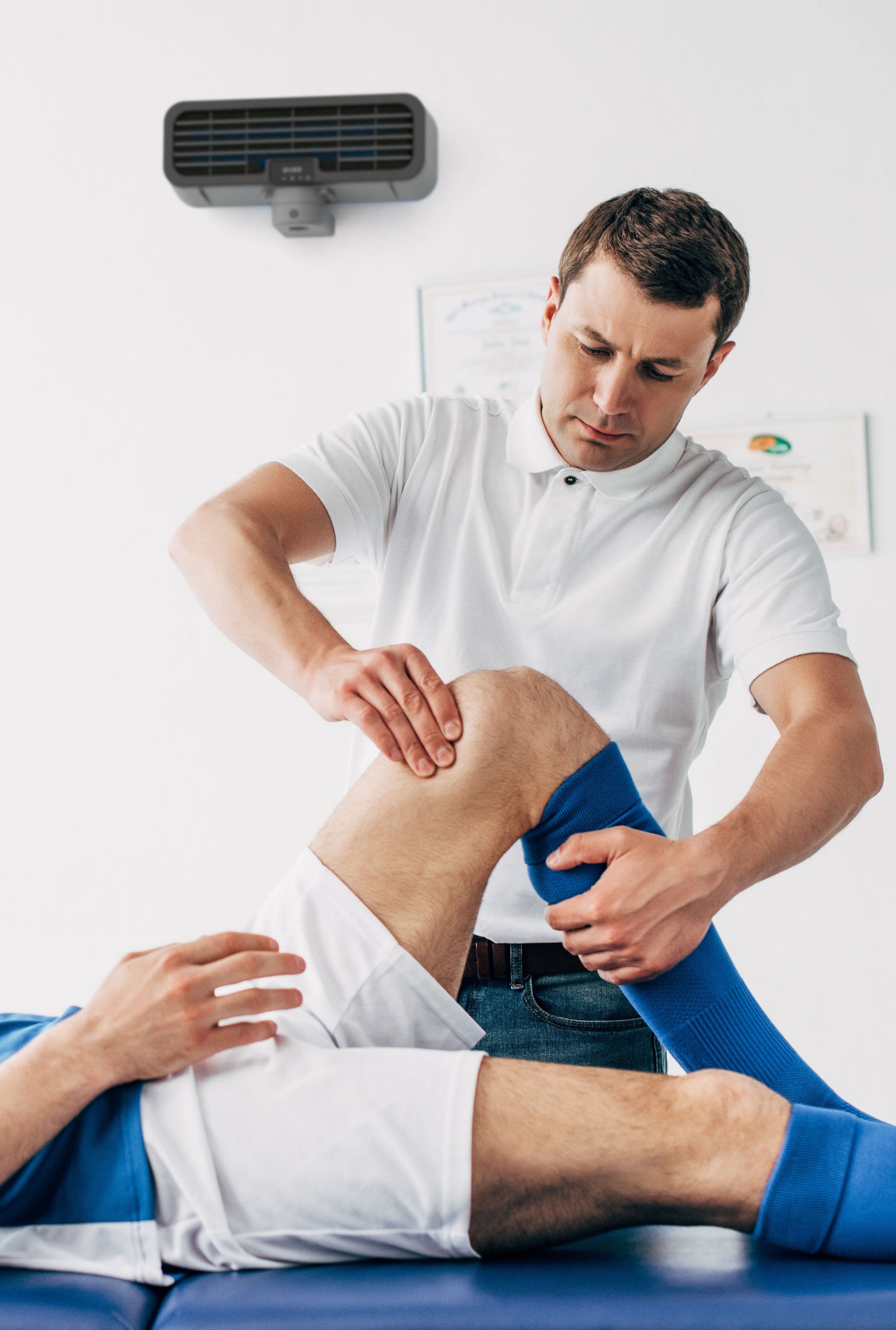 A physio therapist working on a patients knee with an ODEO upperviolet unit attached to the wall.