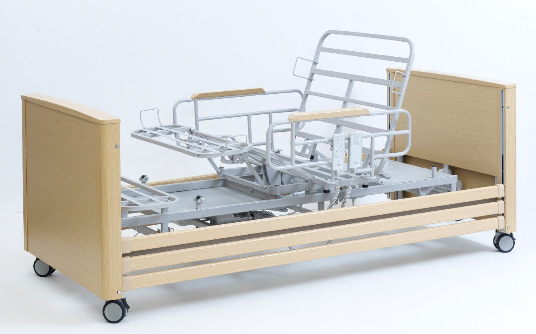 A profiled hospital bed with aluminum side rails and a beige wooden headboard. The bed is equipped with side and back rests, and appears to be electrically operated.